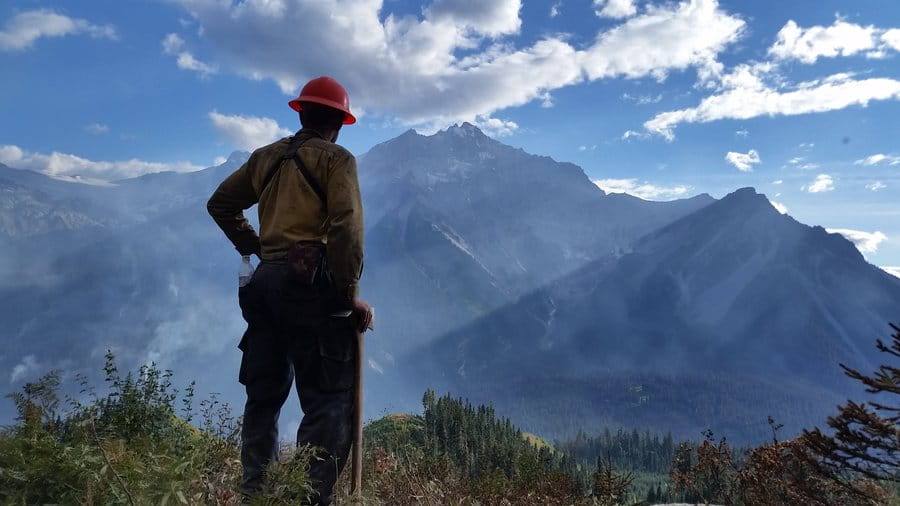 A wildland firefighter surveys the landscape and Mount Currie with smokey skies