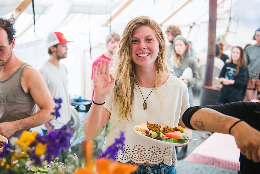 A young woman tree planter stands holding her meal and waving at the camera